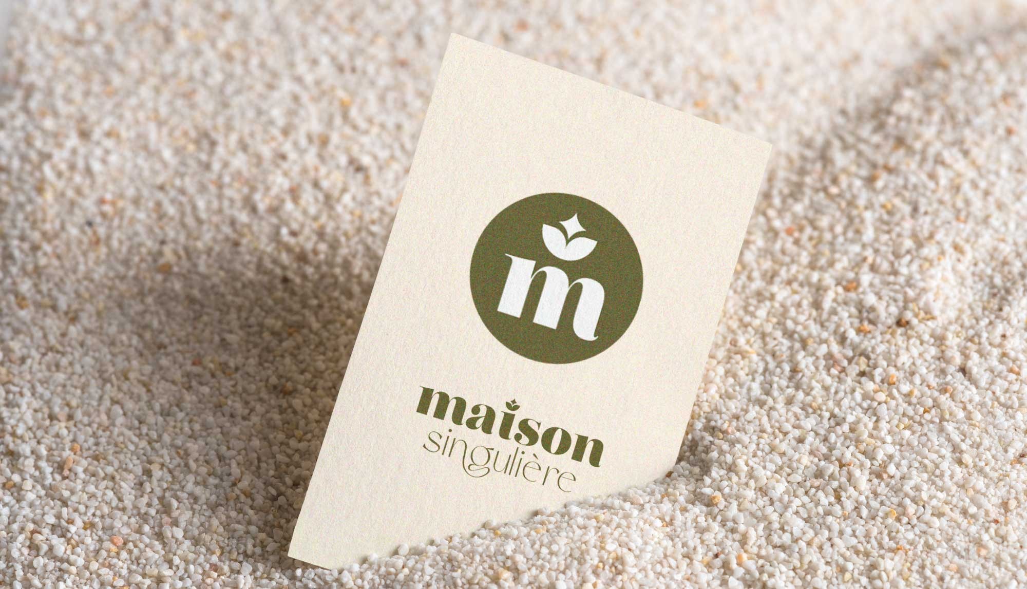 Mise en situation de l'identité visuelle sur une carte de visite de Maison Singulière imprimé en vert/kaki sur papier blanc/crème, travail graphique réalisé par l'agence de communication ÈS.B Studio.